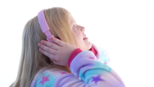 moderne Mode - schönes blondes Mädchen hört Musik mit Kopfhörern und tanzt auf weißem Hintergrund im kigurumi-Pyjama - isoliert auf weiß - Filmmaterial, Video