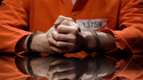 Prisoner in handcuffs clenching fists, denying quilt, interrogation room - 写真・画像