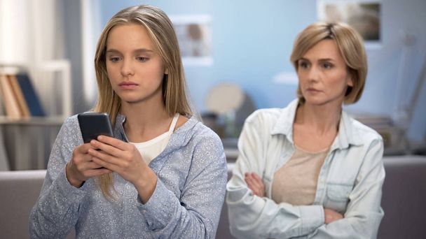 Daughter with smartphone in hands ignoring mom, misunderstanding and conflict - Photo, image