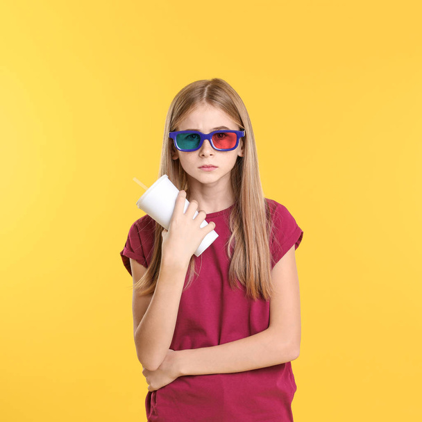 Emotional teenage girl with 3D glasses and beverage during cinema show on color background - Фото, изображение