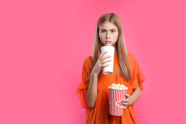 Emotional teenage girl with popcorn and beverage during cinema show on color background - Foto, imagen