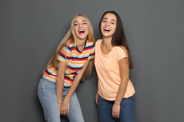 Mujeres jóvenes riendo juntas sobre fondo gris
 - Foto, Imagen