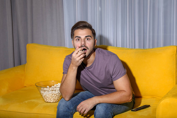 Emotional man watching with popcorn TV on couch in living room - Foto, Imagem