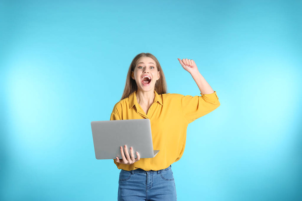 Emotional young woman with laptop celebrating victory on color background - Φωτογραφία, εικόνα