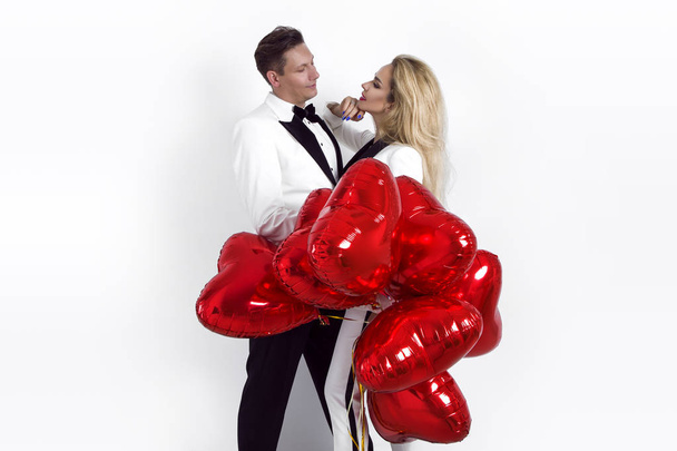 Ευτυχισμένο ζευγάρι όμορφη θέτοντας σε άσπρο φόντο και εκμετάλλευση μπαλόνια καρδιά. Ημέρα του Αγίου Βαλεντίνου. -Εικόνα - Φωτογραφία, εικόνα