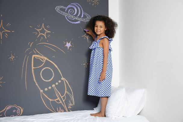 African-American child drawing rocket with chalk on wall in bedroom - Foto, imagen