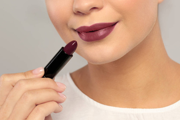 Beautiful woman applying dark lipstick on gray background, closeup - Valokuva, kuva