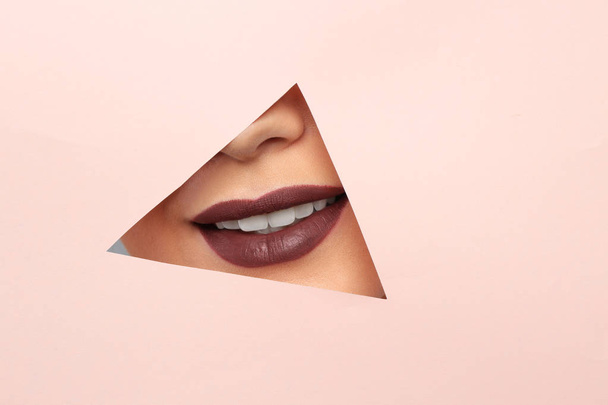 Lips of beautiful young woman with dark lipstick visible through hole in color paper - Valokuva, kuva