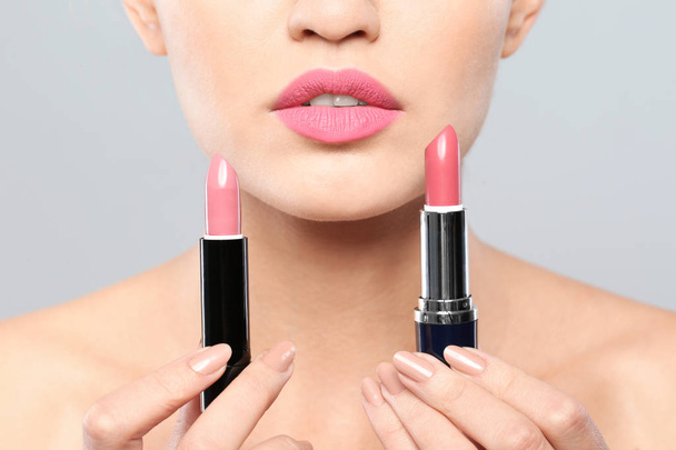 Young woman with lipsticks on gray background, closeup - Foto, Bild