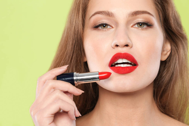 Young woman applying red lipstick on color background - Fotoğraf, Görsel