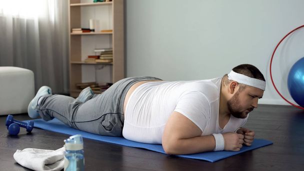 Человек с избыточным весом лежит на спортивном матче, собирается делать упражнения на доске, тренировки
 - Фото, изображение