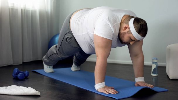 Fat male trying to do push up exercise at home, weak muscles, lack of motivation - Fotó, kép
