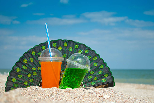 Twee cocktails fan zand close-up op de achtergrond van de zee en hemel, wolken, fan, stilleven drinken glazen buis, drinken van vloeibare soda, zomer zon weekend rust, vakantie kust Golf schuim schelpen - Foto, afbeelding