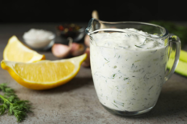 Glass jug of Tzatziki cucumber sauce with ingredients on table. Space for text - Fotó, kép
