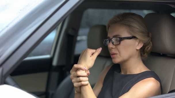 Attractive woman in eyeglasses sitting in car, suffering from wrist pain, health - Фото, изображение