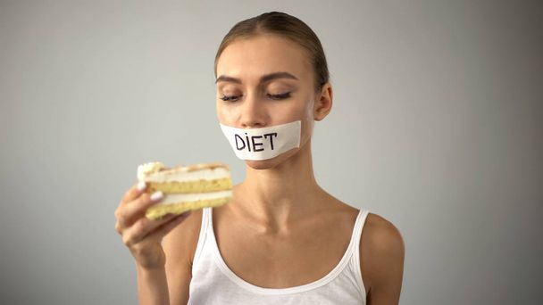 Woman with taped mouth looking at cake, fighting temptation to eat pie, diet - Fotoğraf, Görsel