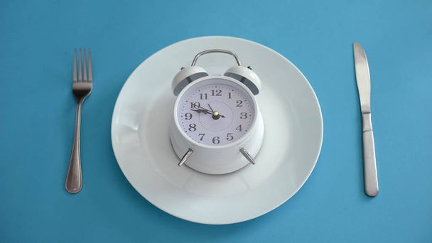 Alarm clock on plate, adhere to diet time, proper nutrition, discipline, closeup - Foto, afbeelding