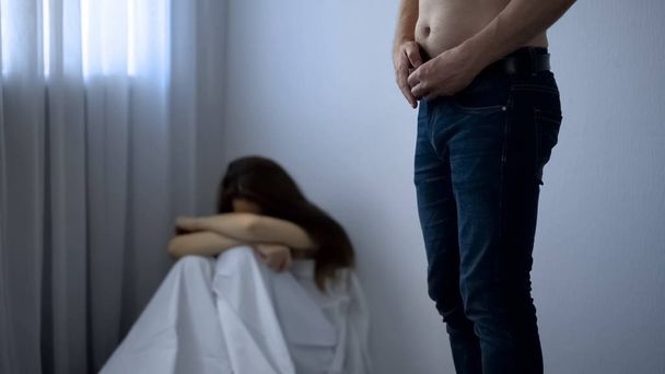 Man fastening belt on pants leaving frightened girl in corner, sexual abuse - Valokuva, kuva
