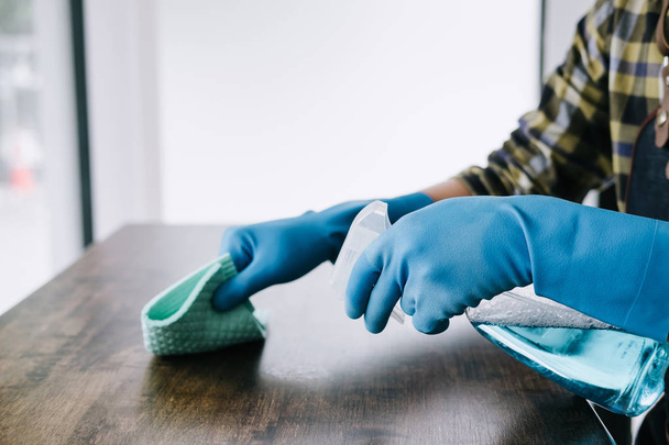 Husband housekeeping and cleaning concept, Happy young man wiping dust using a spray and a duster while cleaning on table at home. - Foto, Imagen