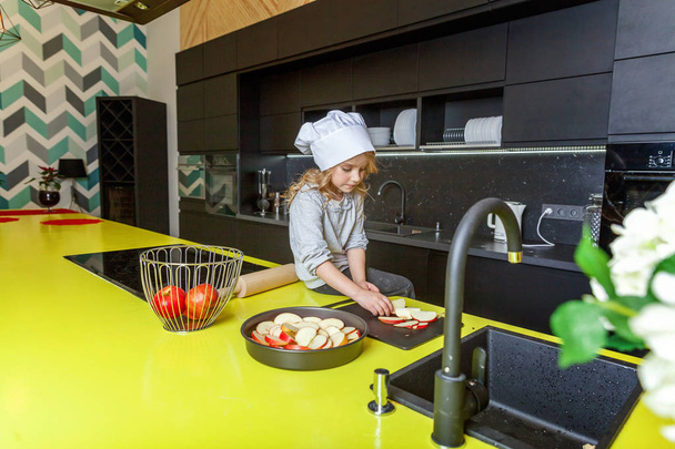 Κοριτσάκι με καπέλο σεφ προετοιμάζει ψήνουμε μηλόπιτα σπιτικό διακοπών στην κουζίνα. Παιδί μαγείρεμα υγιή τρόφιμα στο σπίτι και τη διασκέδαση. Παιδική ηλικία, νοικοκυριό, ομαδική εργασία βοηθώντας έννοια - Φωτογραφία, εικόνα