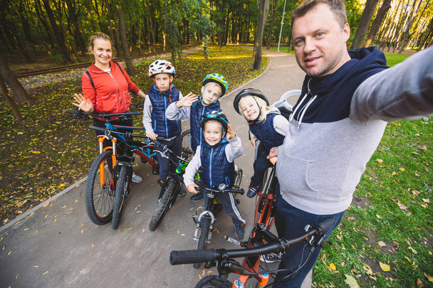 The theme family sports outdoor recreation. large family Caucasian 6 people mom dad and 4 children three brothers and sister ride bicycles in park on bicycle path. Father holds camera makes photo. - Photo, Image