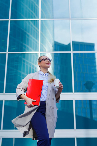 Business woman holds in her hands folder with documents and cup of coffee. Businesswoman standing next to the business center - Photo, Image