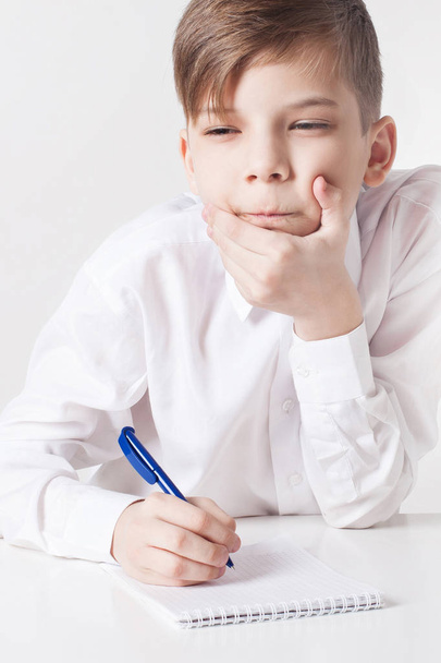 Chłopiec szkoły zamyślony pisze w notesie na stole. Koncepcja edukacji - Zdjęcie, obraz