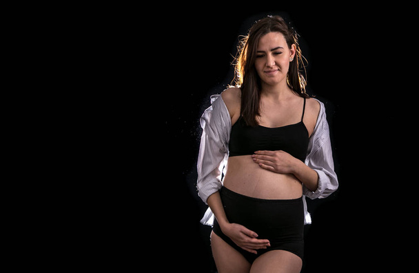 Retrato de mujer embarazada sobre fondo negro, concepto de embarazo y en anticipación de un niño
 - Foto, imagen