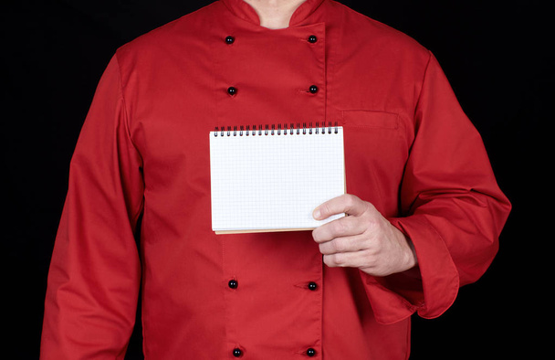 chef in red uniform  holding a blank notebook, black background - 写真・画像