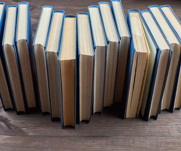 stack of books in a blue cover on a brown wooden table, top view - Fotó, kép