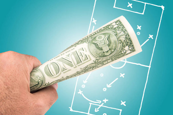 a white man holding dollar banknote with the picture of soccer footbal filed with play tactics and strategy drawn on light blue background - 写真・画像