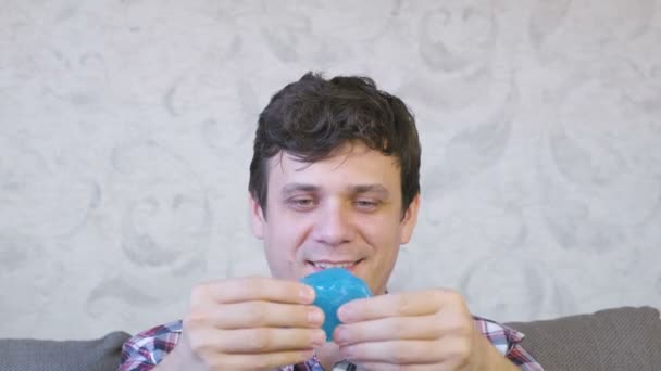 Playful man is stretching a blue slime sitting on the coach and playing. - Filmmaterial, Video