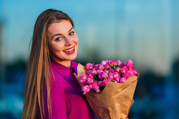 beautiful woman smiles at camera holding bunch of pink roses - Foto, Imagen