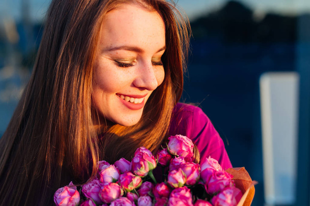 збуджена дівчина з довгим волоссям посміхається на її букет кущових троянд
 - Фото, зображення