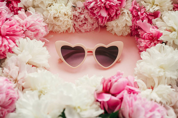 Μοντέρνα καρδιά σχήμα ροζ γυαλιά ηλίου με ροζ και λευκές παιώνιες σε παστέλ ροζ χαρτί. Κομψό Γεια καλοκαιρινή εικόνα. Διεθνής ημέρα γυναικών. Ημέρα του Αγίου Βαλεντίνου. Καλοκαιρινές διακοπές - Φωτογραφία, εικόνα