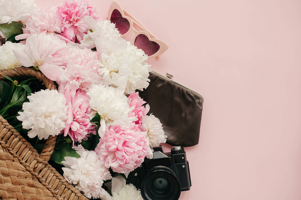 Stylish  pink peonies in straw bag, photo camera, purse, retro sunglasses on pastel pink paper with copy space. International Women's Day. Hello spring. Summer vacation concept. Flat lay - Photo, Image