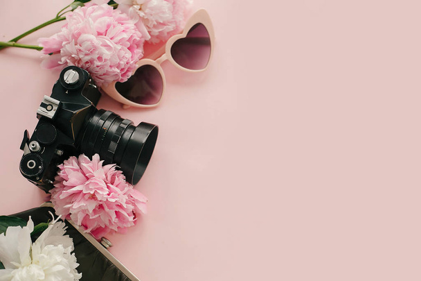 Pink sunglasses, photo camera and vintage purse with pink and white peonies on pastel pink paper. Flat lay with copy space. Hello spring. Summer vacation. International Womens Day. - Photo, Image