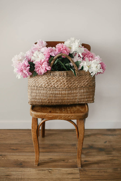 stilvolle rosa und weiße Pfingstrosen im Strohsack auf einem rustikalen Holzstuhl im Zimmer. Weltfrauentag. glücklicher Muttertag. Hallo Frühling. schöner Strauß. Leben auf dem Land - Foto, Bild