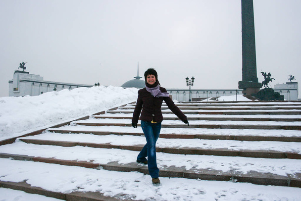 A young woman on the stairs in the winter park. Happy woman jumping on the snow. - Фото, зображення