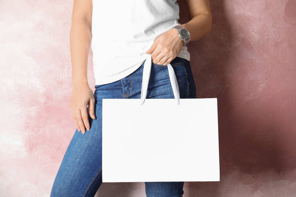 Woman holding mock-up of paper shopping bag on color background - Фото, изображение