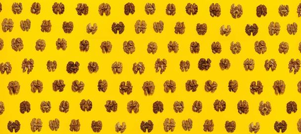 Mitades de nueces en líneas con sombra dura sobre fondo amarillo, imagen plana
. - Foto, imagen