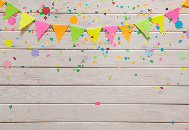 Colored flags garland with confetti against white wooden background  - Foto, afbeelding