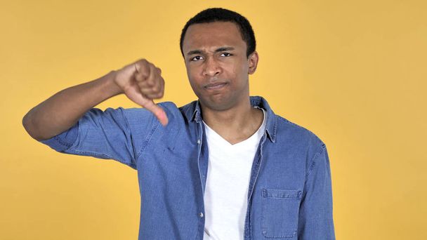 Afrikaanse jongeman gebaren duim omlaag geïsoleerd op gele achtergrond - Foto, afbeelding
