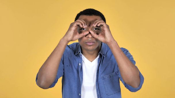 黄色の背景に分離された手作りの双眼鏡を使って検索アフリカ青年 - 写真・画像