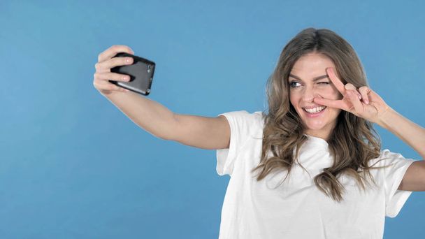 Gelukkig jong meisje nemen Selfie terwijl geïsoleerd op blauwe achtergrond - Foto, afbeelding