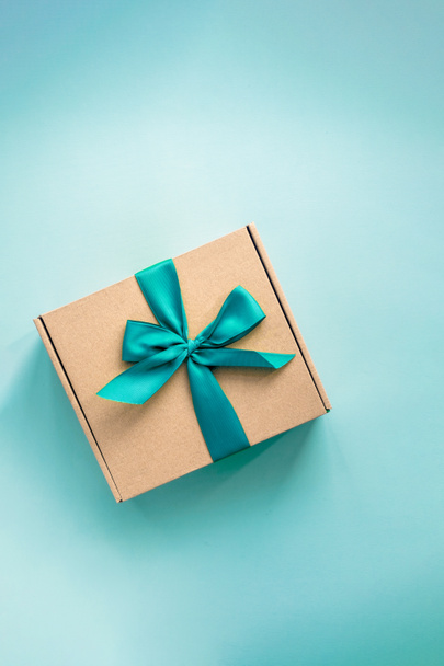 One craft paper box  with green ribbon bow on blue background from above. Minimalism, copy space - Photo, Image