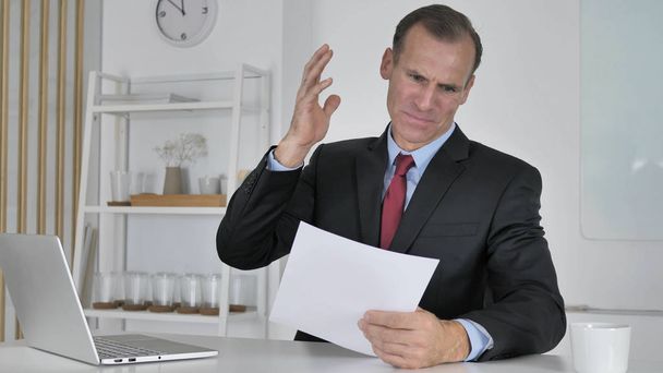 Dühös középső éves üzletember reagál a veszteséget, miközben olvasási dokumentumokban - Fotó, kép