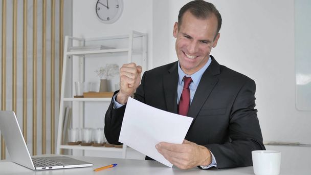 Excited Middle Aged Businessman Celebrating Success while Reading Documents - Foto, imagen