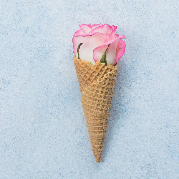 Creative minimalism flat lay with waffle cone and pink roses on blue background. Valentines day, Mother and Spring concept - Foto, imagen