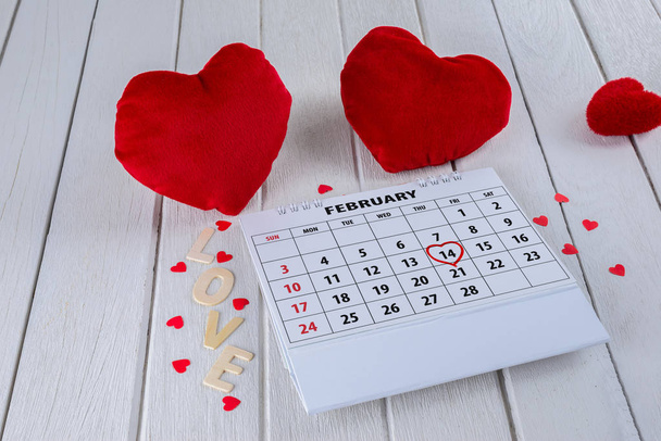 Calendar page with red hand written heart highlight on February 14 of Saint Valentines day with red Heart shape and Wooden letters word "LOVE" on white wooden table - Photo, Image